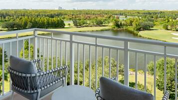 En balkon med fletstole og et lille bord, med udsigt over en golfbane og en sø.