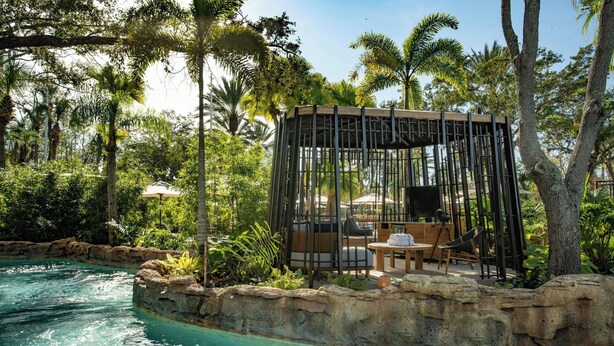 A poolside area with a wooden gazebo, lounge chairs, and a table.
