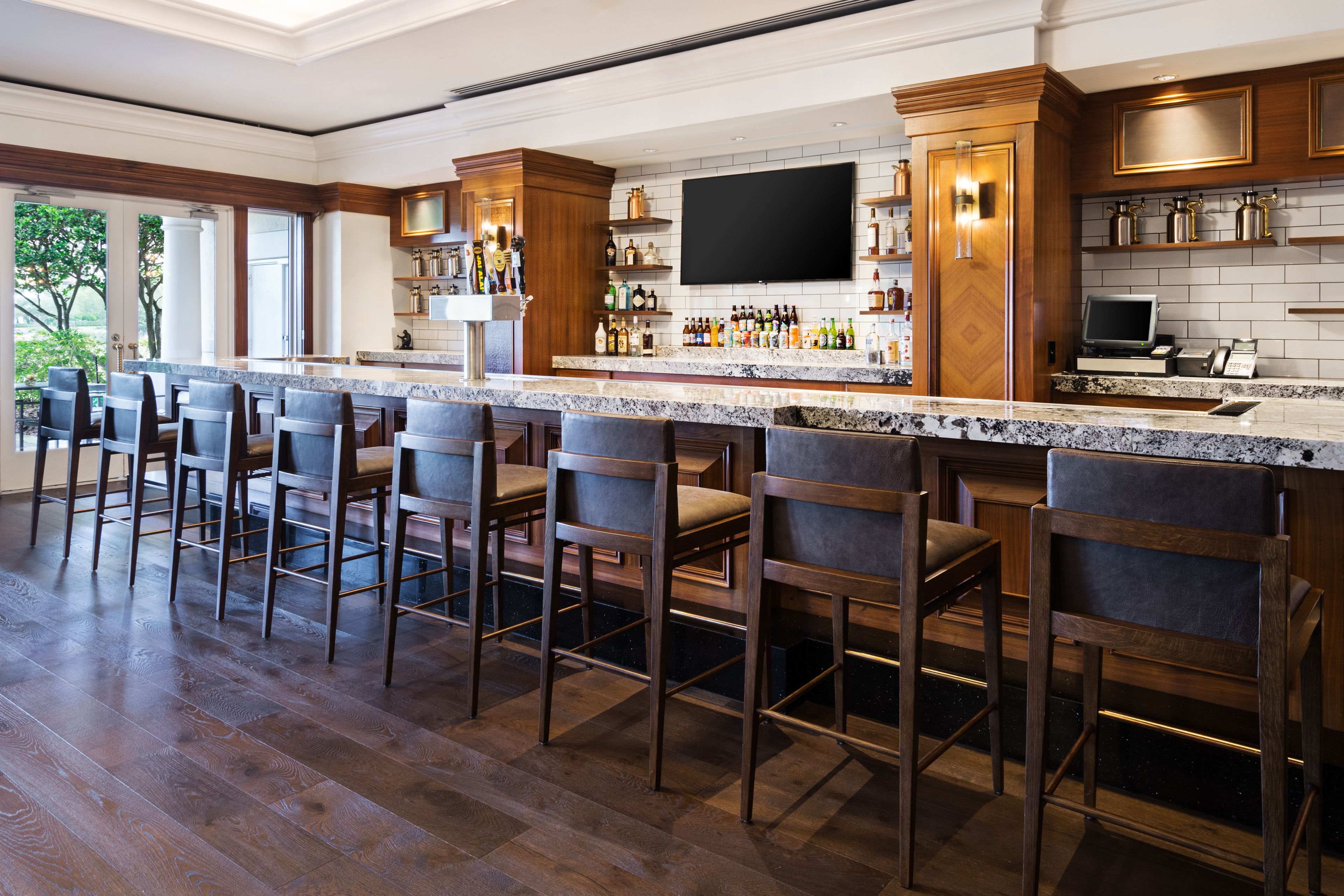 Un espace bar doté de tabourets en bois, d’un comptoir en granit et d’un téléviseur à écran plat fixé au-dessus du bar.