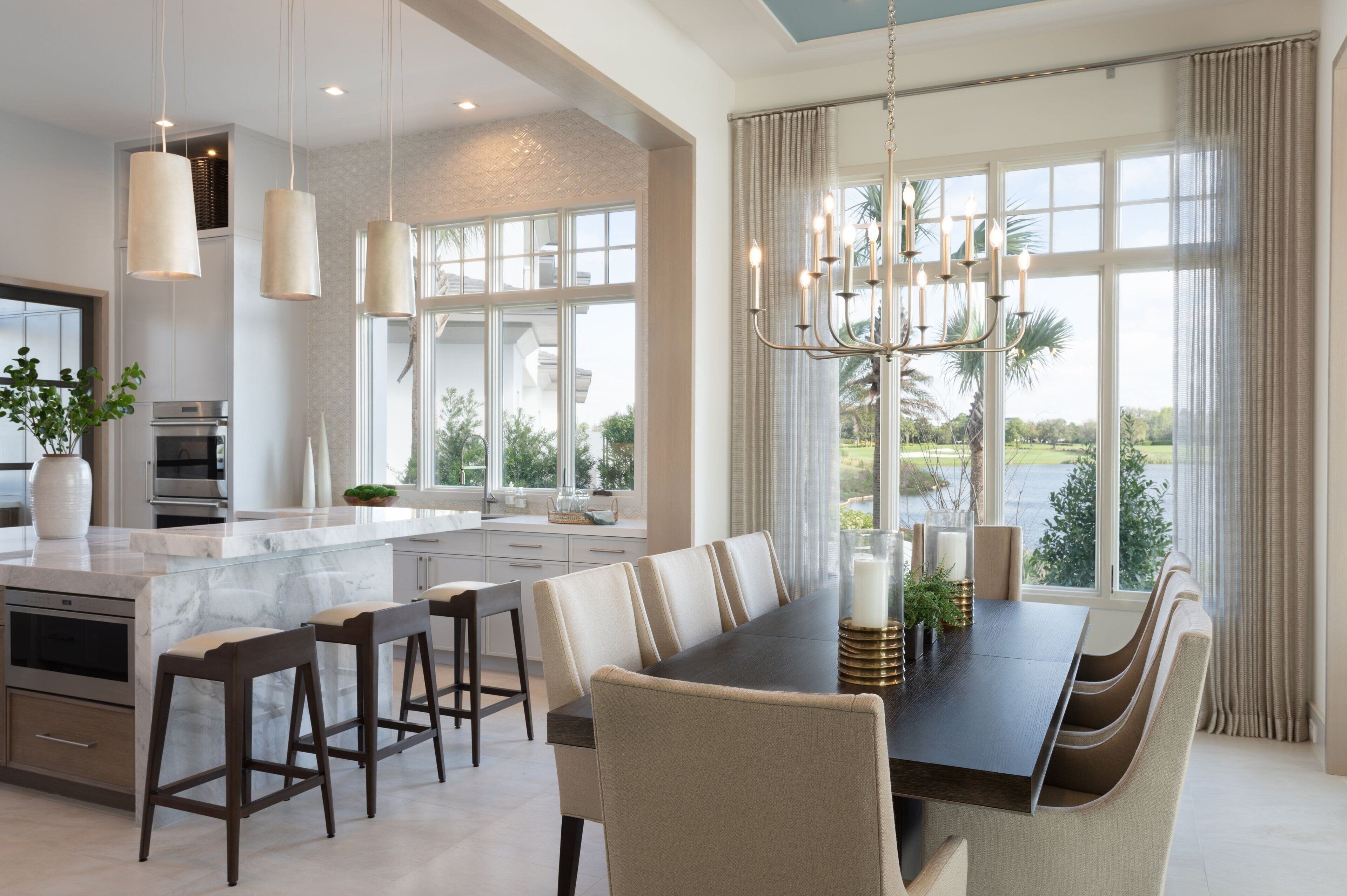 Une cuisine spacieuse dotée d’un grand îlot central, de luminaires suspendus modernes et d’un coin repas avec une longue table et des chaises.