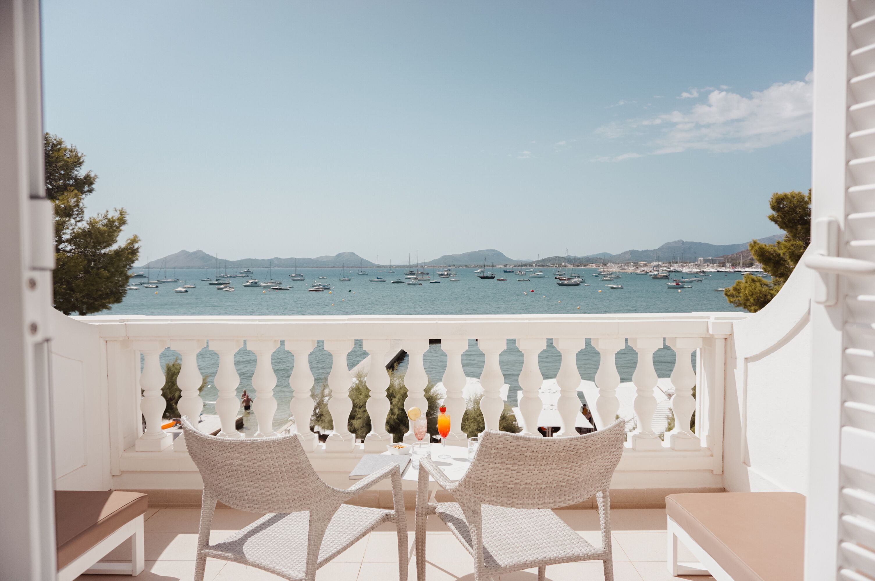 A balcony with white wicker furniture and a view of the sea with boats.