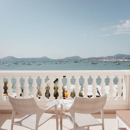 A balcony with white wicker furniture and a view of the sea with boats.