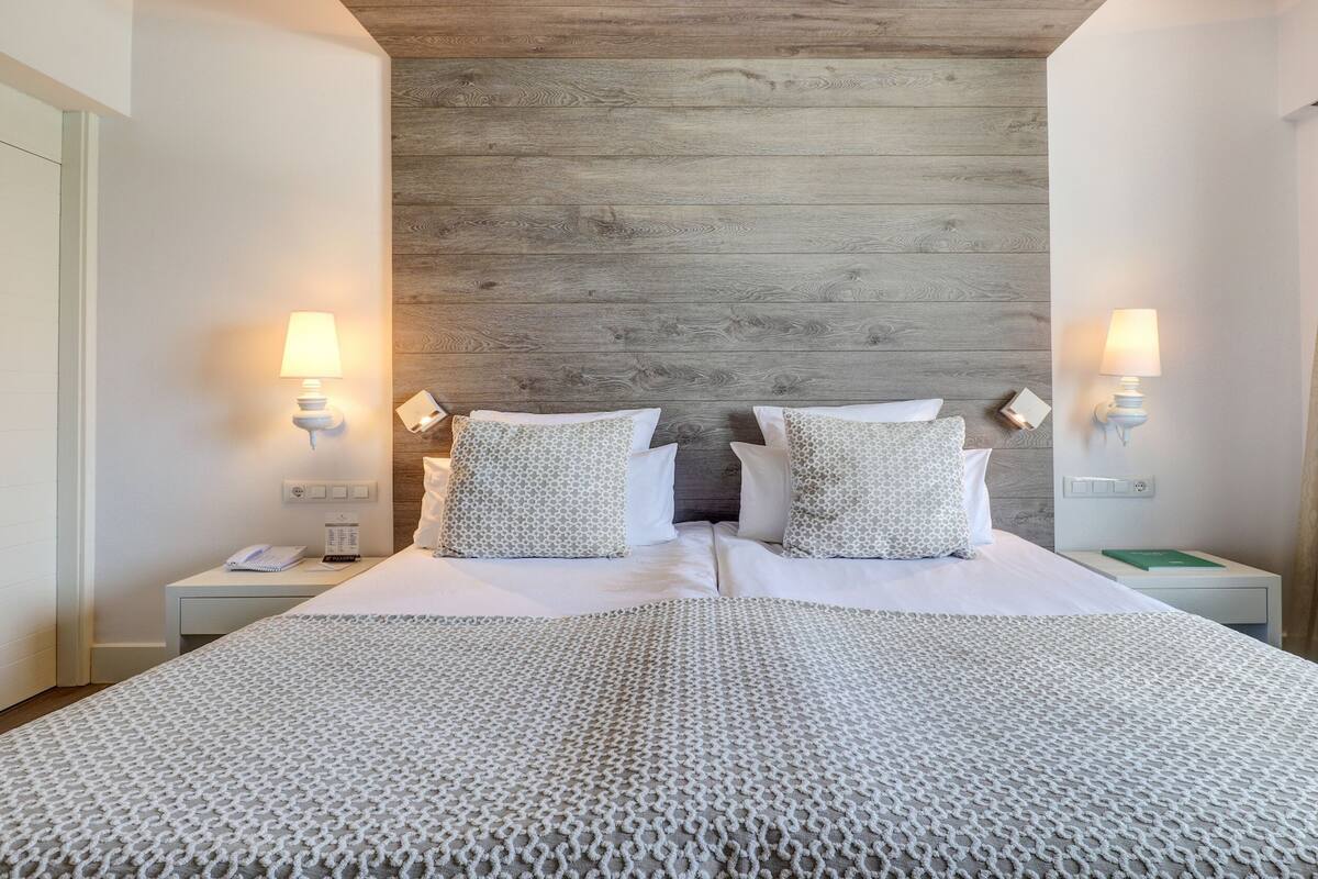 A hotel room with a large bed, two bedside tables, a wooden headboard, and two wall-mounted lamps.