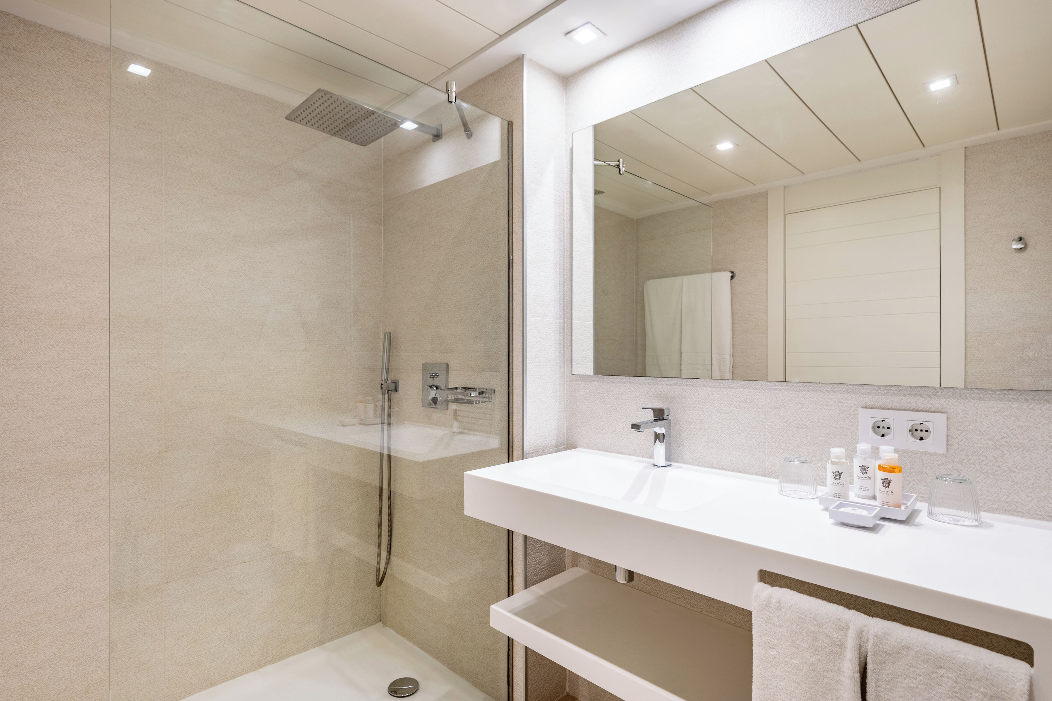 A modern bathroom with a glass-enclosed shower, a white sink with a mirror above, and toiletries on the countertop.