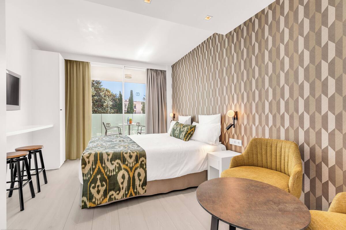 A modern hotel room with a large bed, a sofa, a dining table, and a balcony with a view of the city.