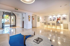 A modern hotel lobby with a reception desk, seating area, and framed artwork on the walls.