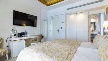 Habitación de hotel con cama, escritorio, silla, televisor, armario y baño con espejo.