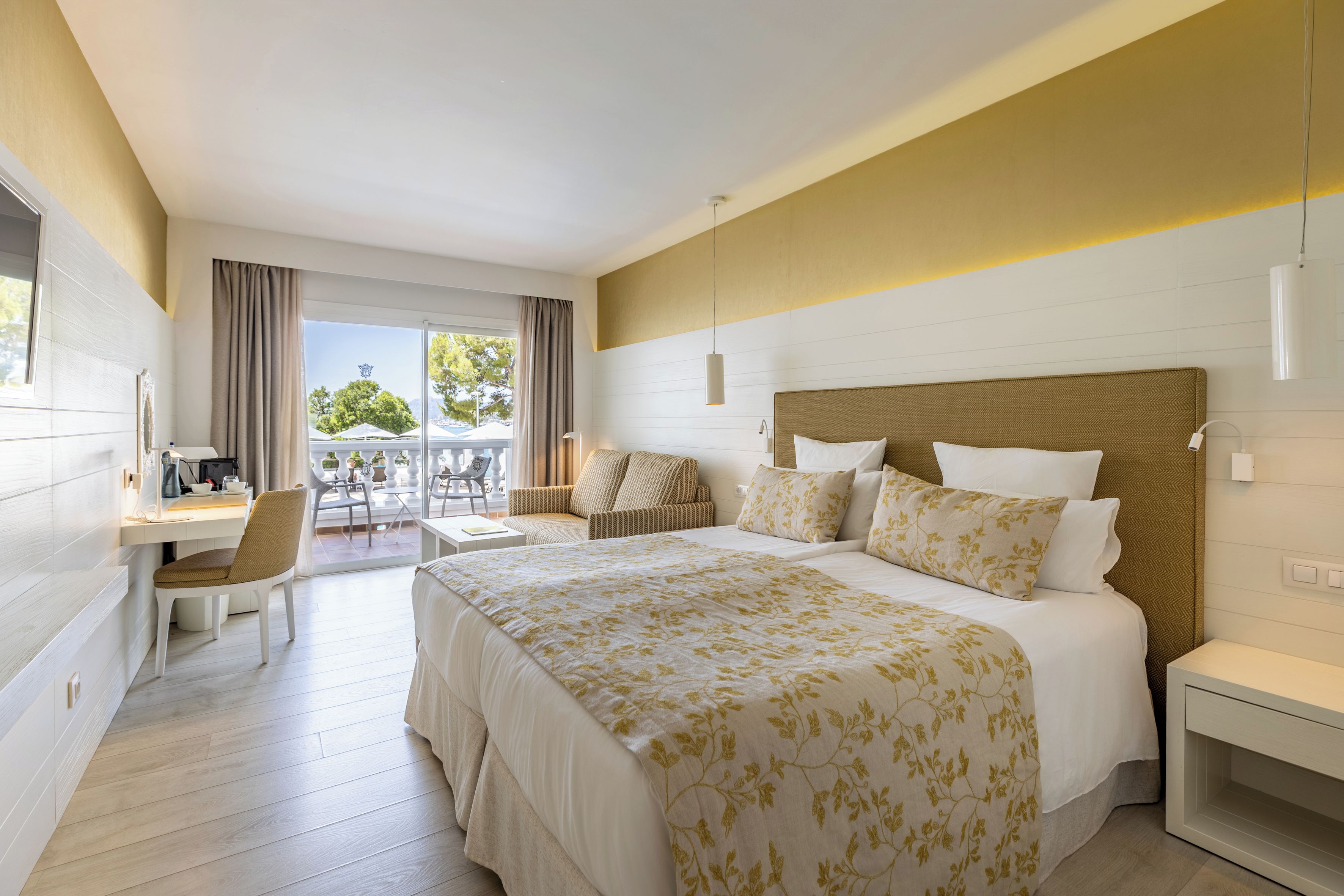 A hotel room with a large bed, a desk, a chair, and a balcony with outdoor seating.