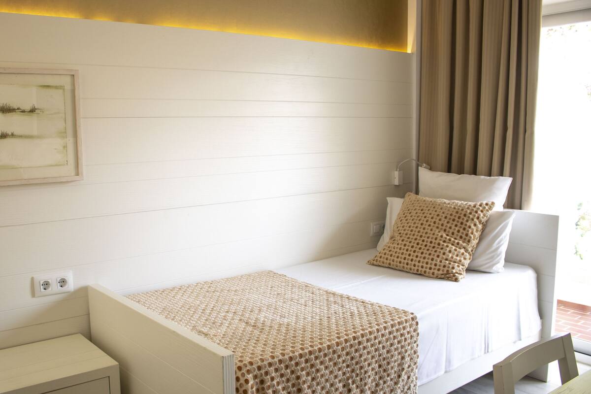 A neatly arranged bedroom with a bed, bedside table, and a wall-mounted power outlet.