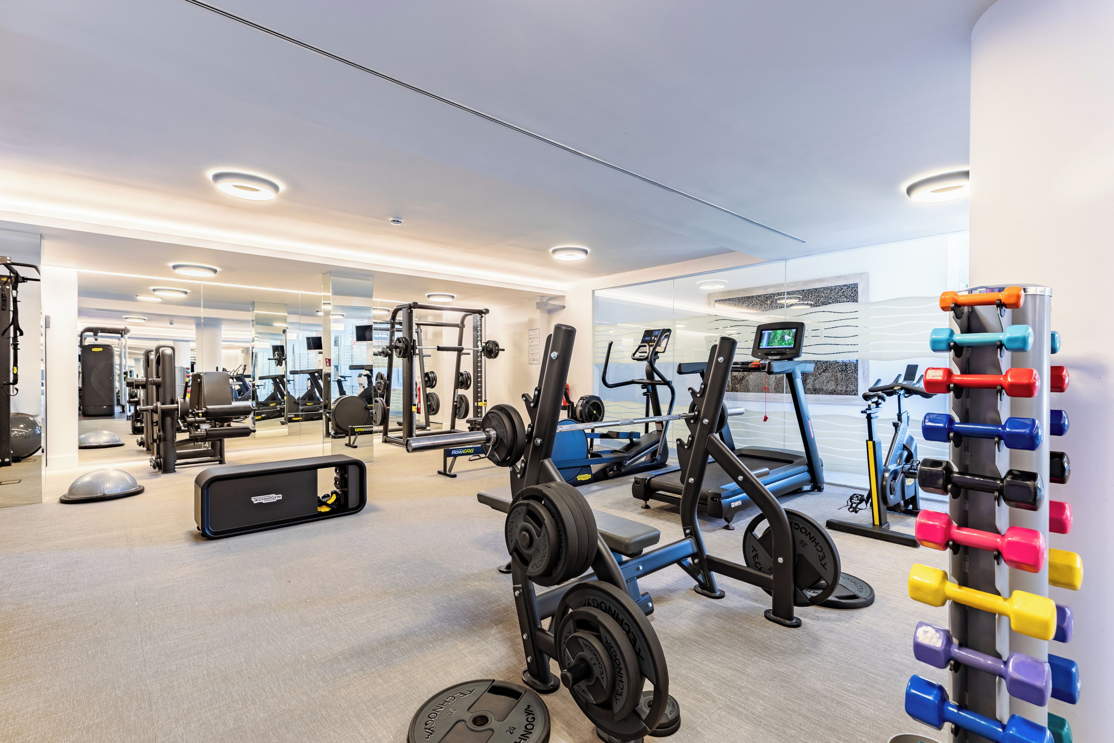 Une salle de sport moderne équipée de divers appareils d’exercice, notamment un rameur, un banc de musculation et des poids libres.