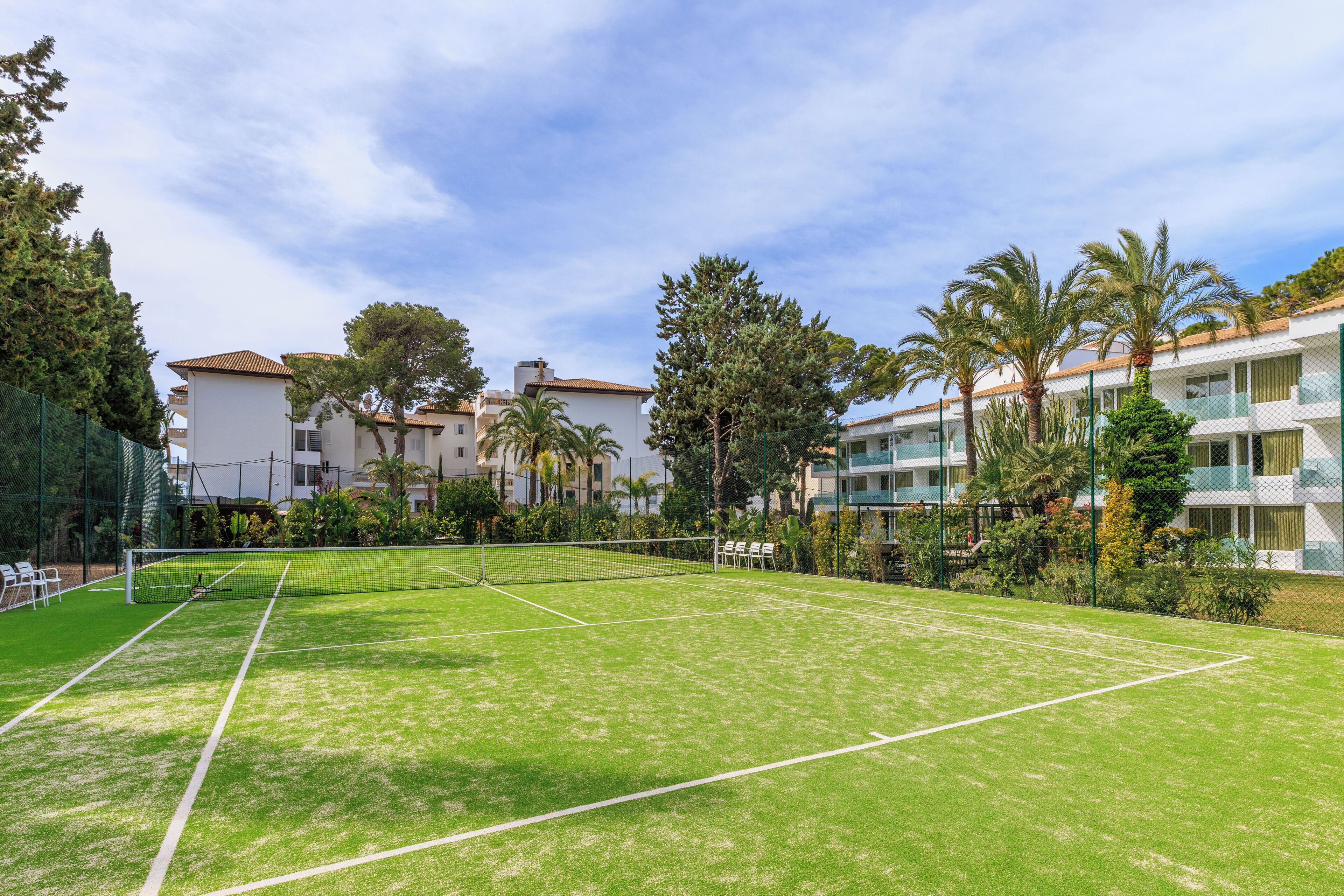 A tennis court with a net, surrounded by greenery and residential buildings.