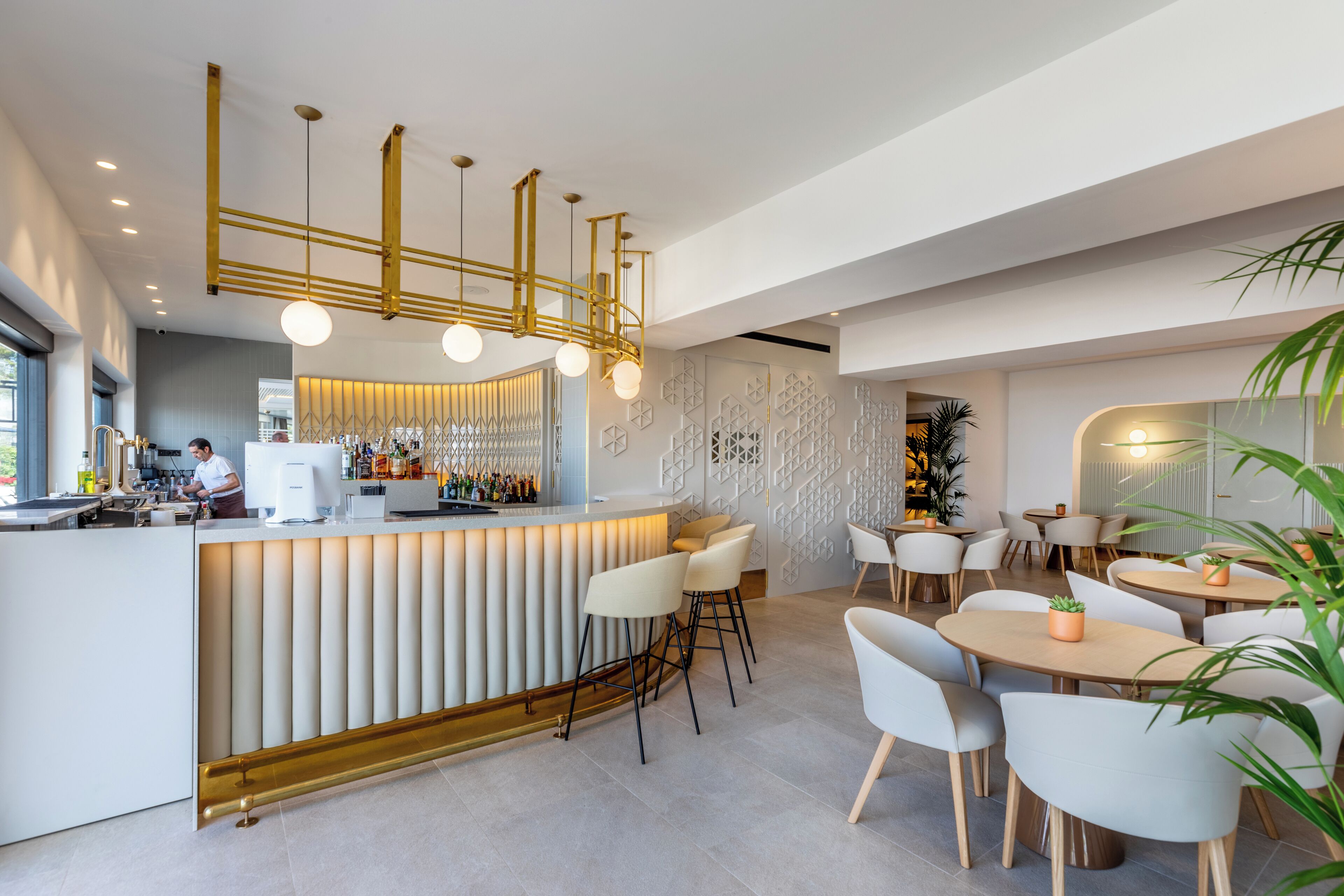 Un área de bar moderna con mostrador blanco, taburetes y una lámpara geométrica única.