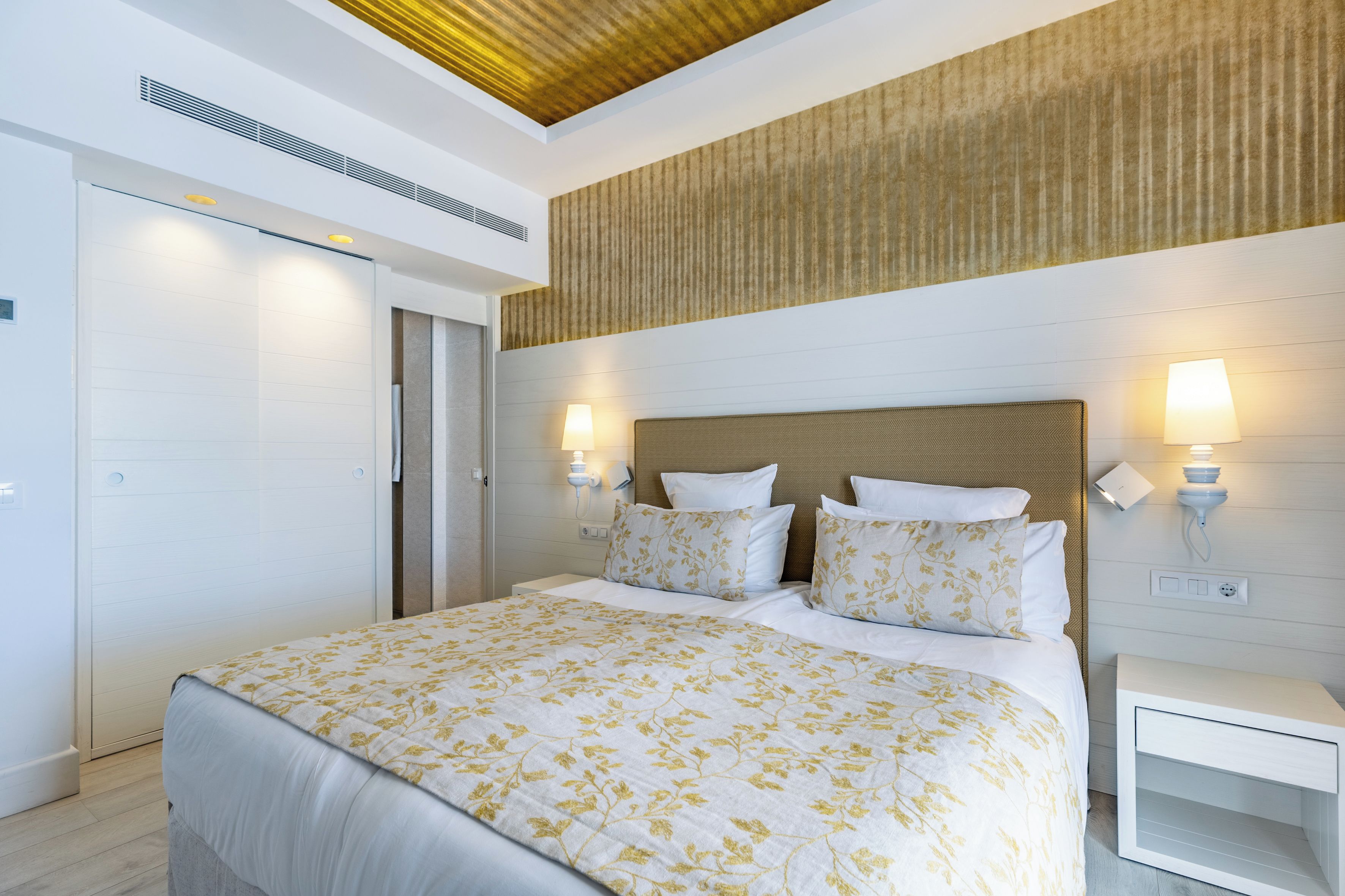 A hotel room with a bed, bedside lamps, a nightstand, and a wooden ceiling.