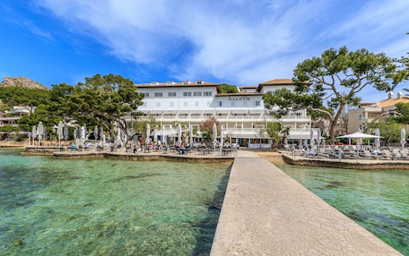 A waterfront hotel with clear blue waters, outdoor seating areas, and a prominent building labeled "ILLA D'OR".
