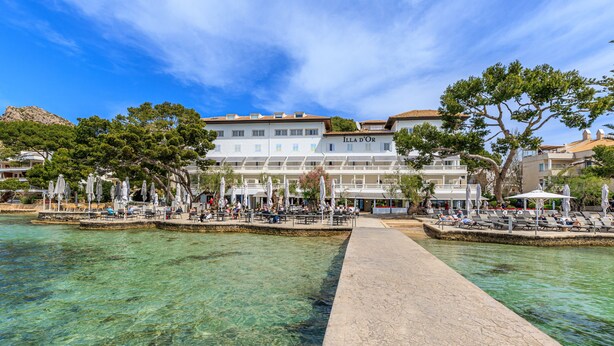 A waterfront hotel with clear blue waters, outdoor seating areas, and a prominent building labeled "ILLA D'OR". - Hotel Illa D'Or (Pollenca)