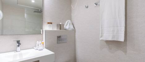 A modern bathroom with a white sink, mirror, and toilet. There is a towel rack with a white towel hanging, and toiletries are placed on the sink.
