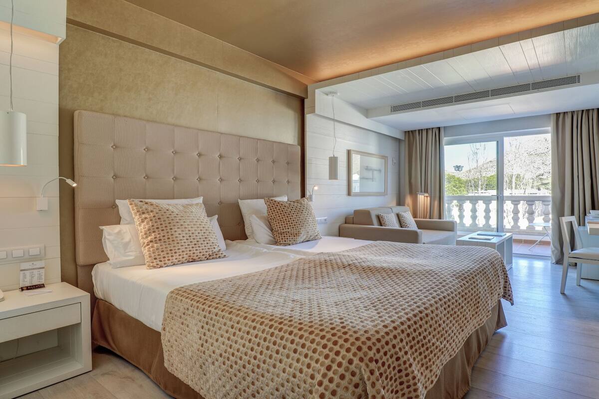 A modern hotel room with a large bed, a desk, and a balcony with a view.