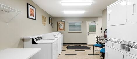 A laundry facility with multiple washing machines, a drying rack, and a seating area with chairs.
