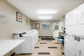 Une buanderie équipée de plusieurs machines à laver, d’un étendoir et d’un espace détente avec des chaises.