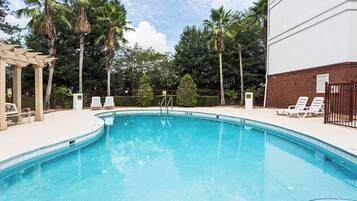 Una piscina con agua cristalina azul, rodeada de sillas reclinables blancas y una pérgola.