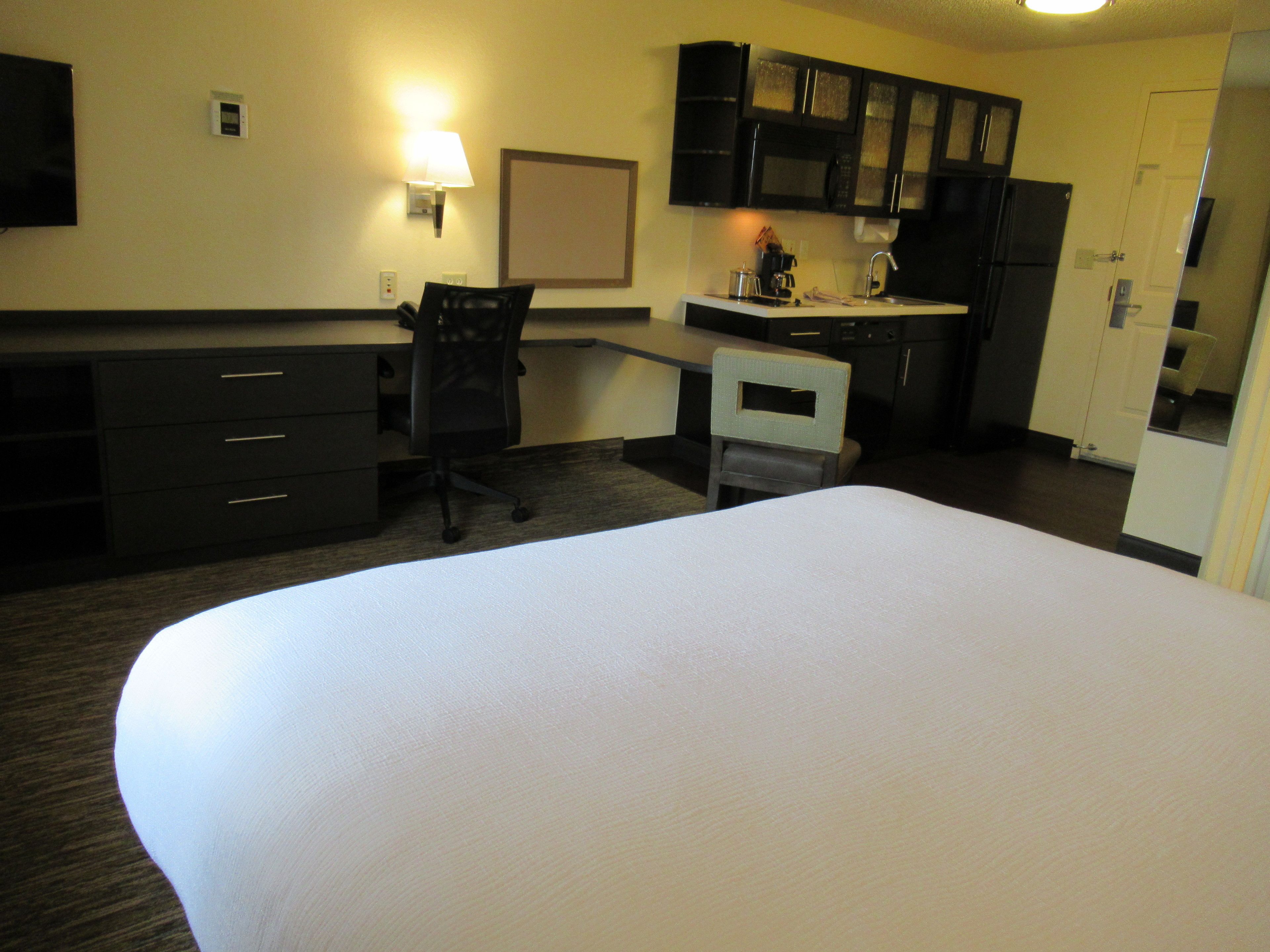 A hotel room with a bed, a desk, a chair, a kitchenette, and a TV.