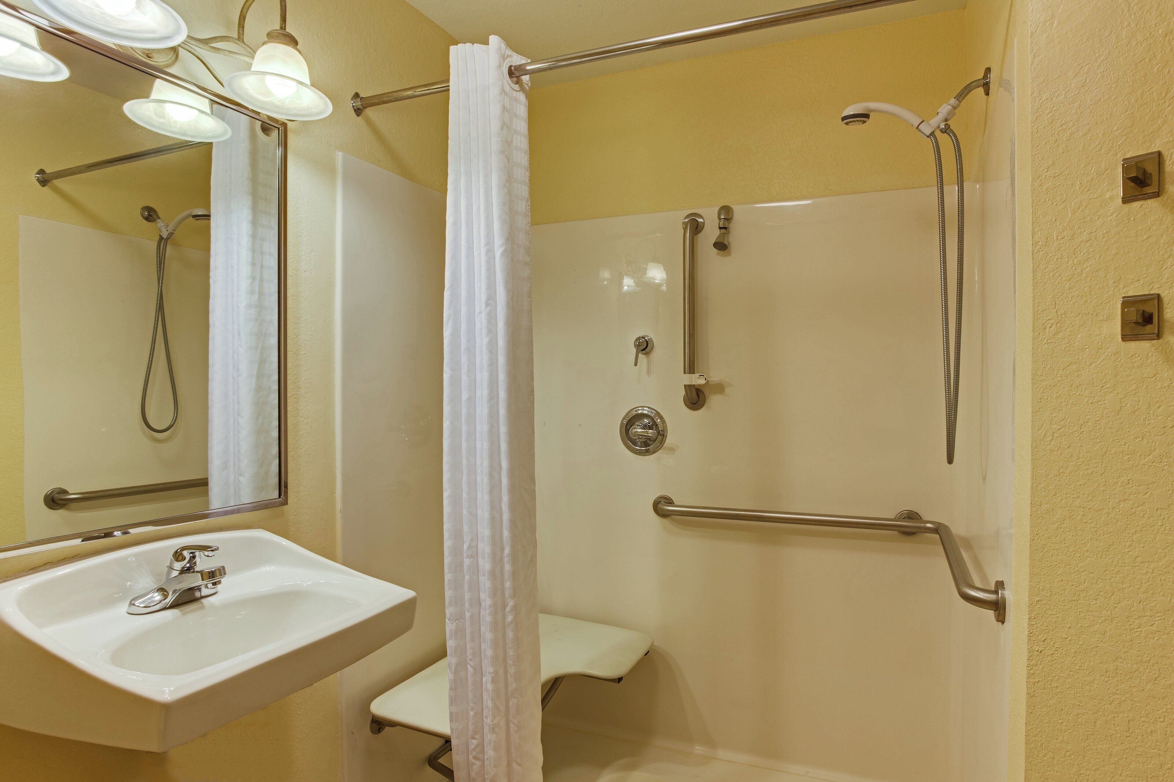 A bathroom with a sink, mirror, shower, and grab bars.