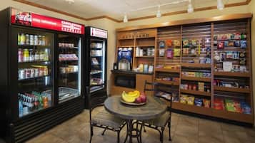 Una barra de aperitivos con dispensadores refrigerados para bebidas, una exhibición de frutas y estantes llenos de diversas opciones de bocadillos y bebidas.