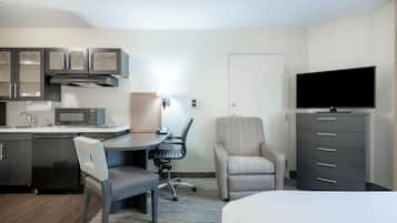 A hotel room with a kitchenette, a desk with a chair, a bed, a TV, and a wardrobe.