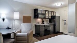 Een kleine hotelkamer met kitchenette, een eethoek met tafel en stoelen, een bed en een lamp.