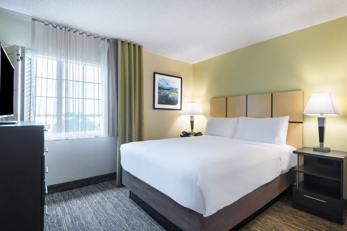 Een hotelkamer met een groot bed, een bureau met lamp, een stoel, een kledingkast en een raam met gordijnen.