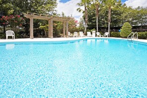 Una piscina azul cristalina con un porche de madera y sillas de descanso blancas.