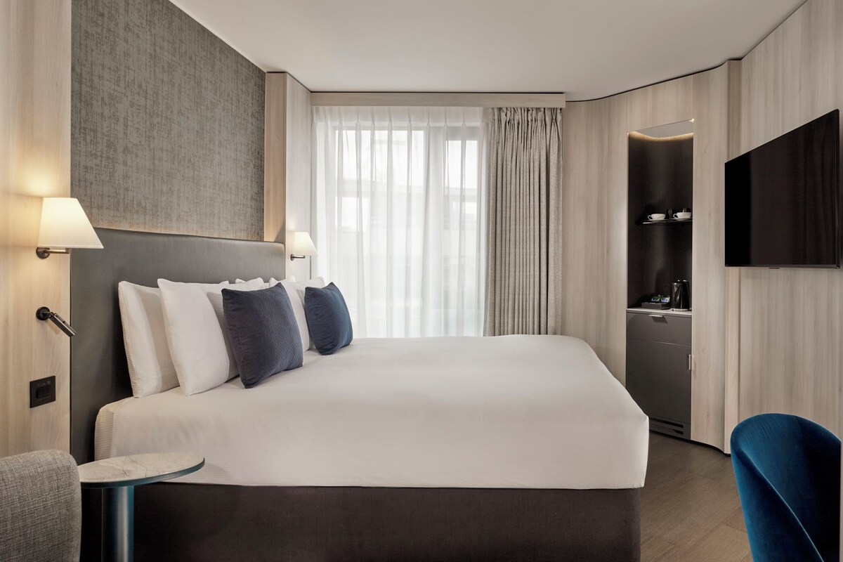 Een moderne hotelkamer met een groot bed, bedlampen, een flatscreen televisie, een klein tafeltje en een stoel.