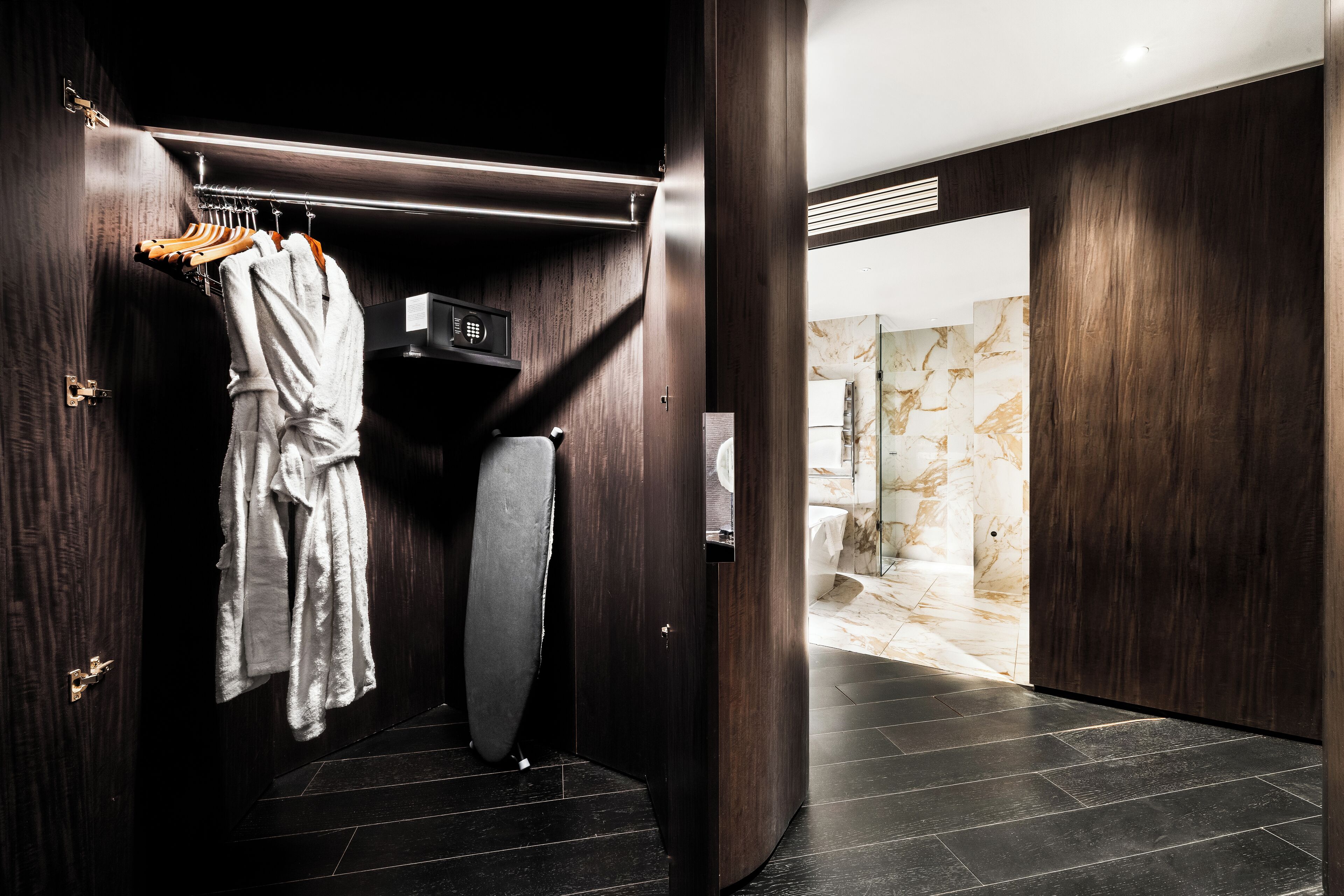 A modern bathroom with dark wood paneling, a marble shower wall, and a robe rack with towels.