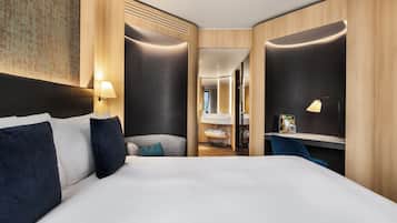 Ein modernes Hotelzimmer mit einem großen Bett, einem Schreibtisch und einem durchgegangene Tür sichtbaren Badezimmer.