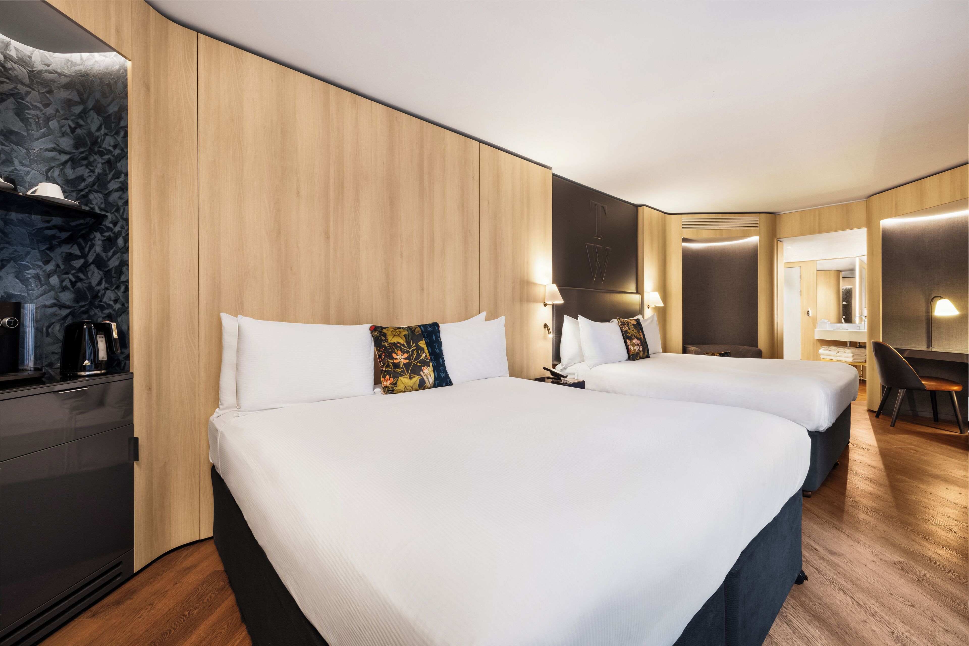 Une chambre d’hôtel avec deux lits, un bureau, une chaise et une armoire.