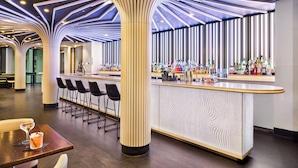 A modern bar area with a curved counter, bar stools, and a unique ceiling design.