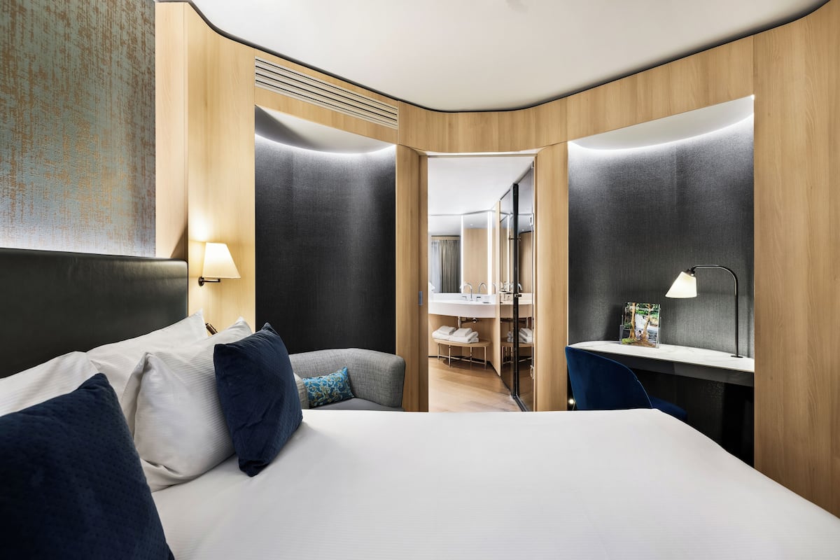 A modern hotel room with a large bed, a desk, and a bathroom visible through an open door.