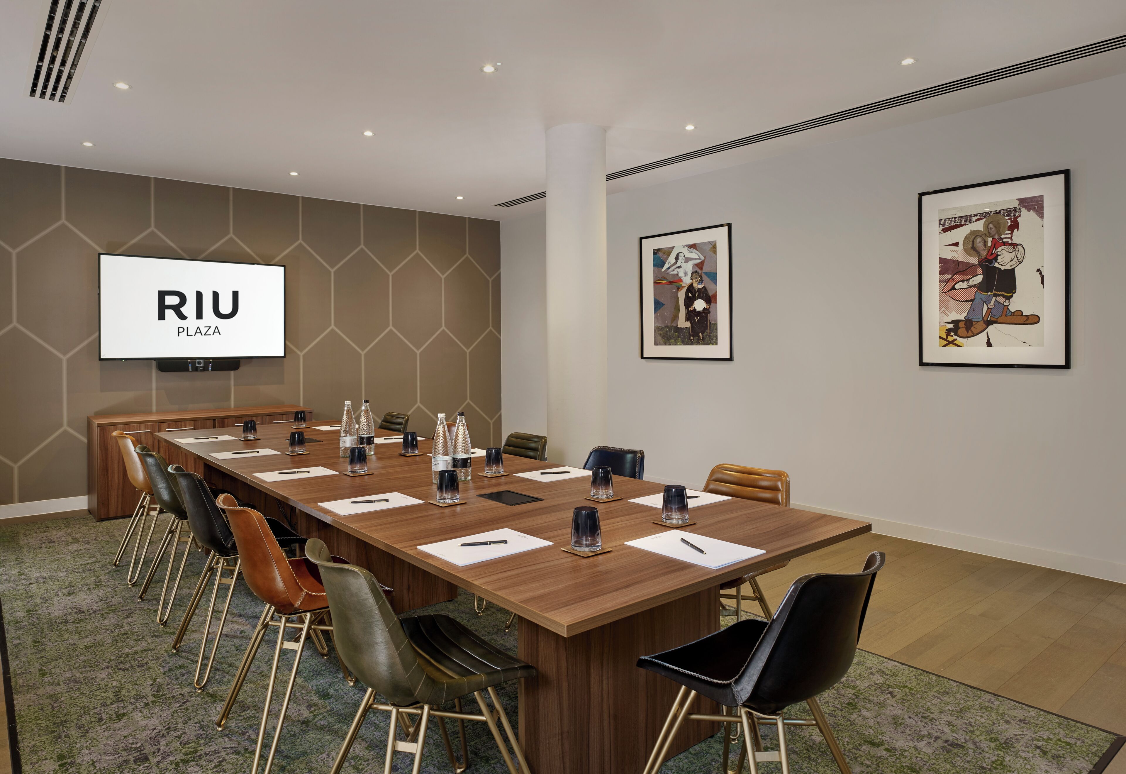 A conference room with a long table, chairs, a TV screen, and artwork on the walls.