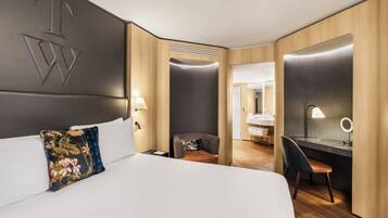 Ein Hotelzimmer mit einem großen Bett, einem Schreibtisch mit Stuhl, einem Spiegel und einem sichtbaren Badezimmer durch eine geöffnete Tür.