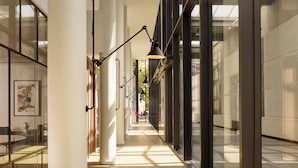 A modern hallway with glass walls, a central light fixture, and a view of the outside.