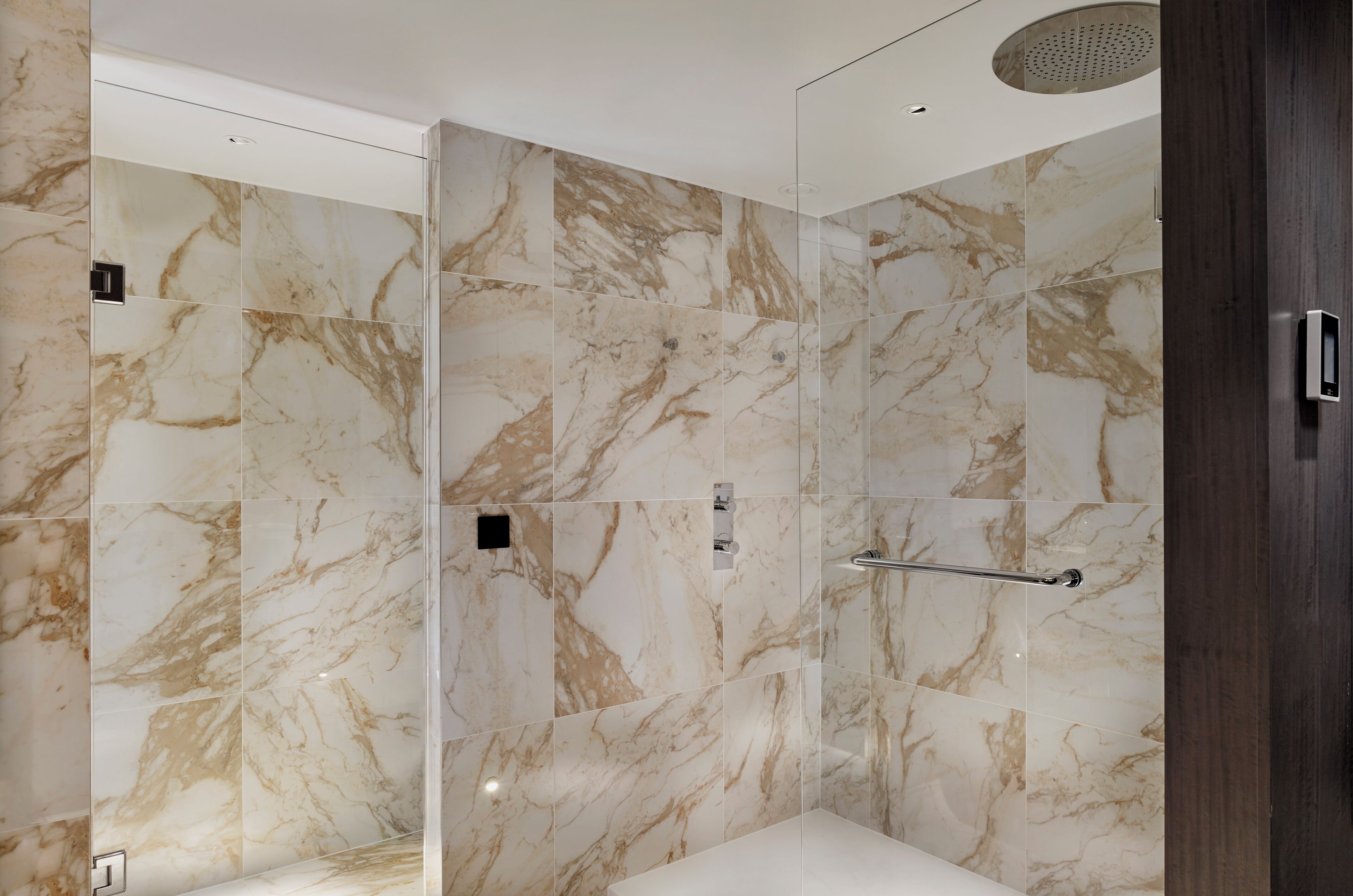 A modern bathroom with marble tiles, a glass shower enclosure, and a wooden door.