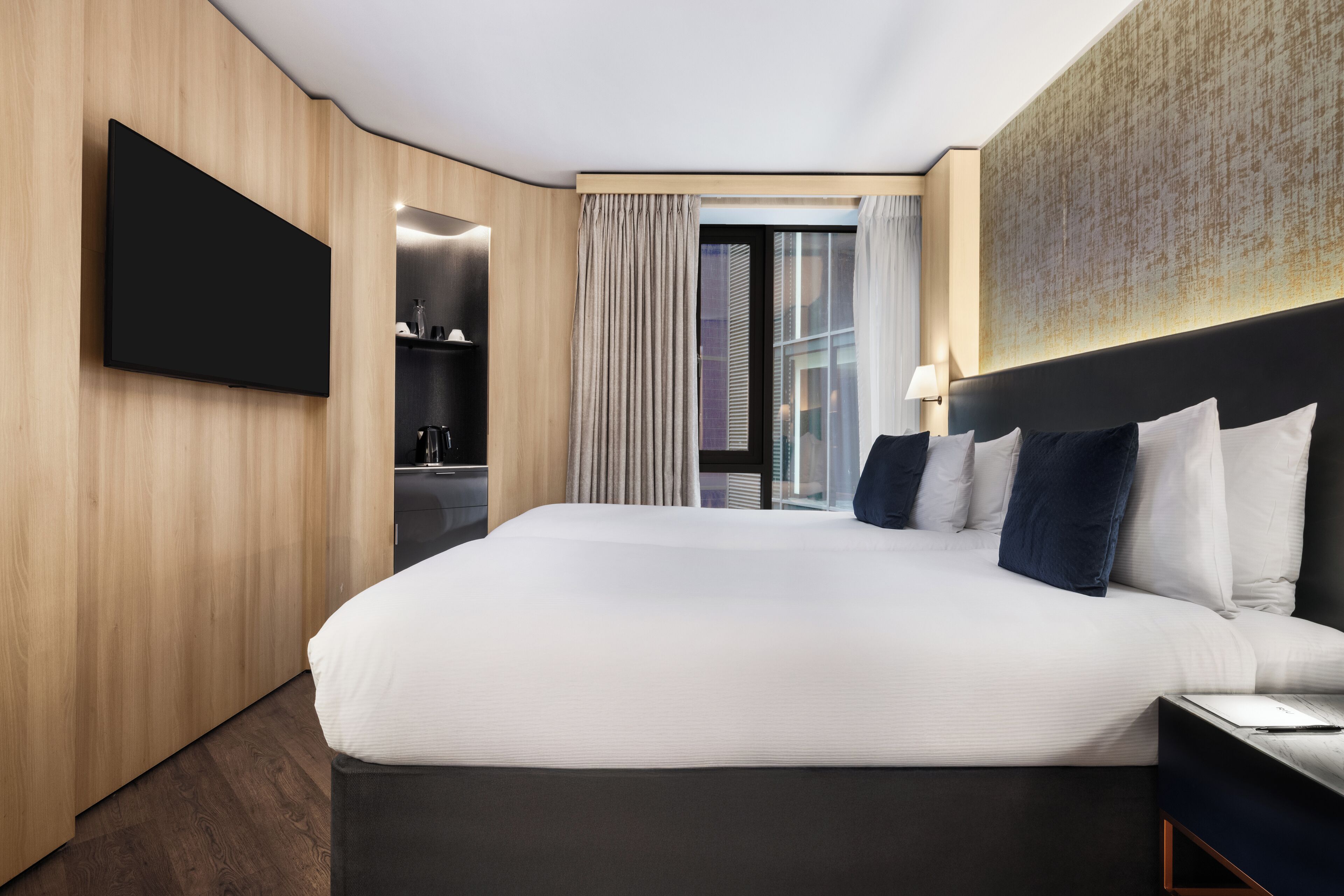 Een moderne hotelkamer met een groot bed, een flatscreen-tv, een bureau met een lamp en uitzicht op de stad.