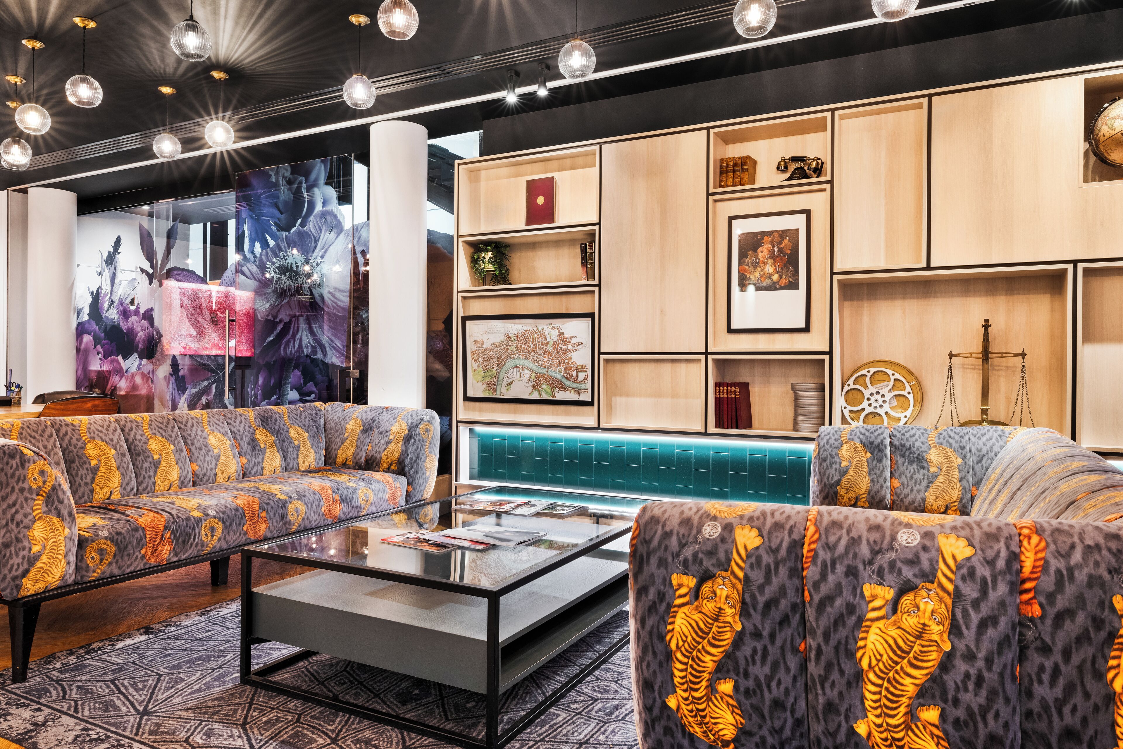 A modern lounge area with sofas, a glass coffee table, and a wall with framed artwork and decorative items.