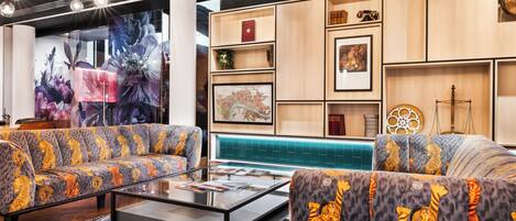 A modern lounge area with sofas, a glass coffee table, and a wall with framed artwork and decorative items.