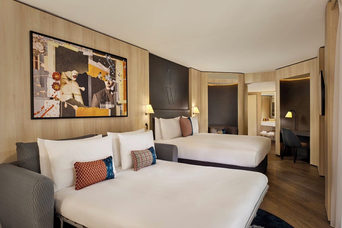Een hotelkamer met twee bedden, een groot abstract schilderij, een bureau en een stoel.