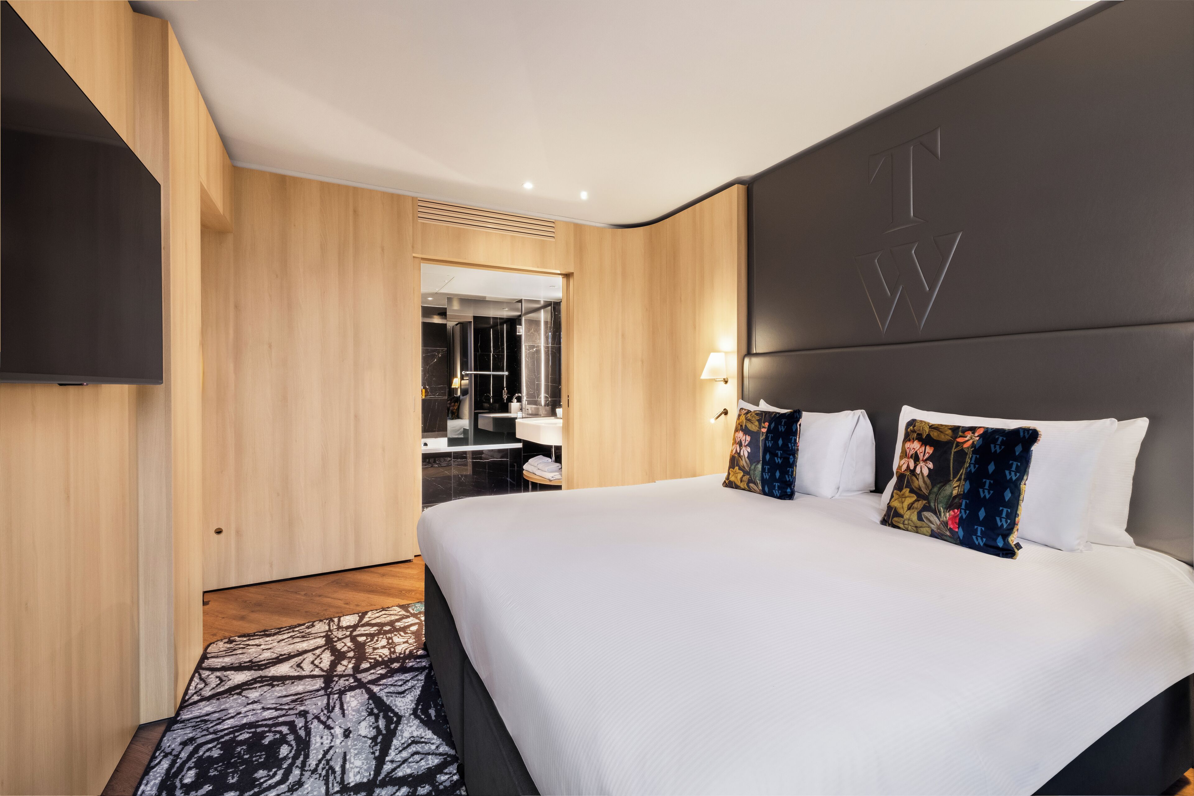 Habitación de hotel moderna con una cama grande, un televisor de pantalla plana en la pared y un diseño de paneles de madera.