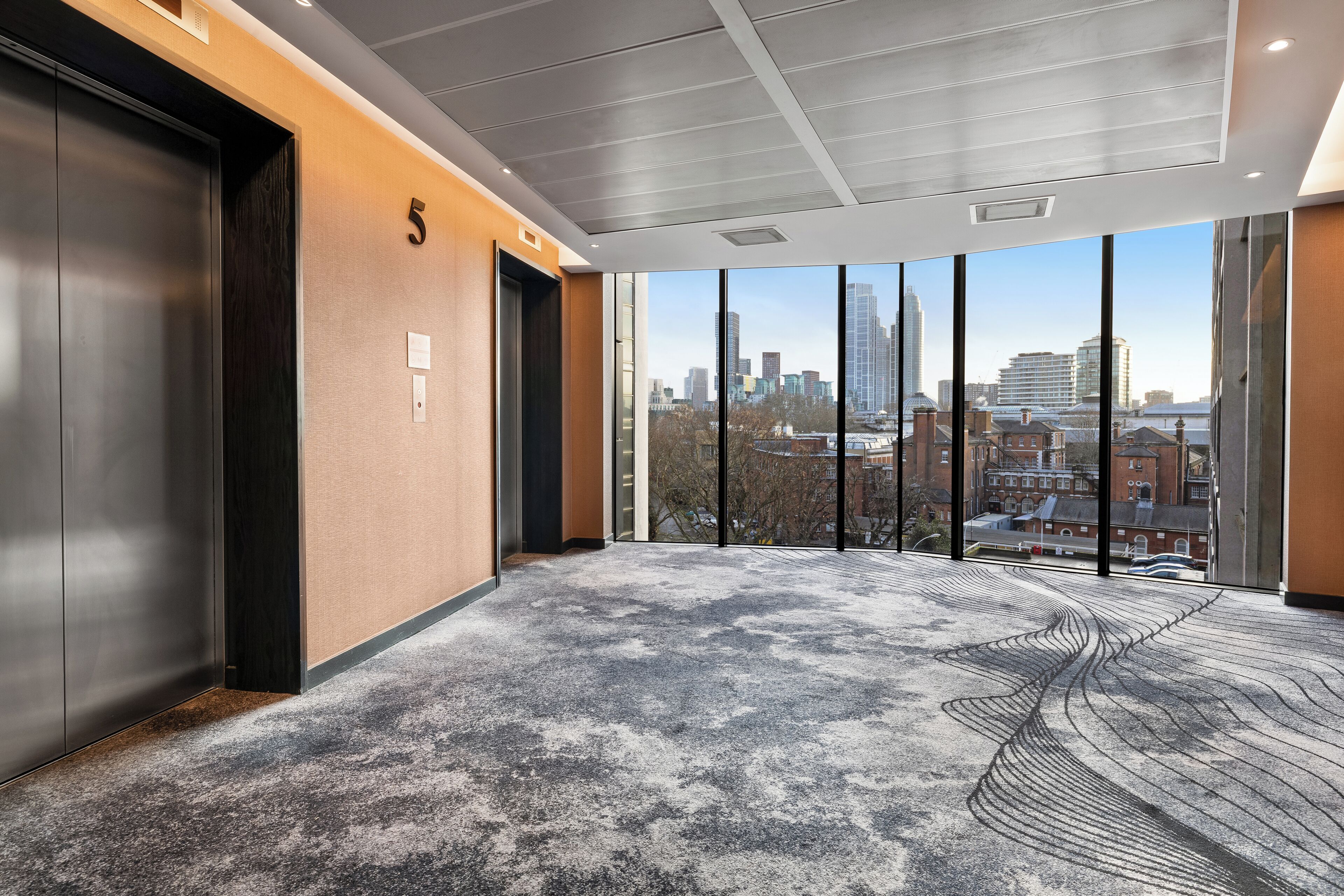 A modern elevator with a city view, a number '5' on the wall, and a patterned carpet.
