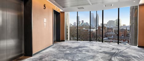 A modern elevator with a city view, a number '5' on the wall, and a patterned carpet.