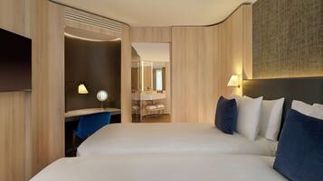 A hotel room with a large bed, a desk with a mirror, a vanity with a sink, and a flat-screen TV mounted on the wall.