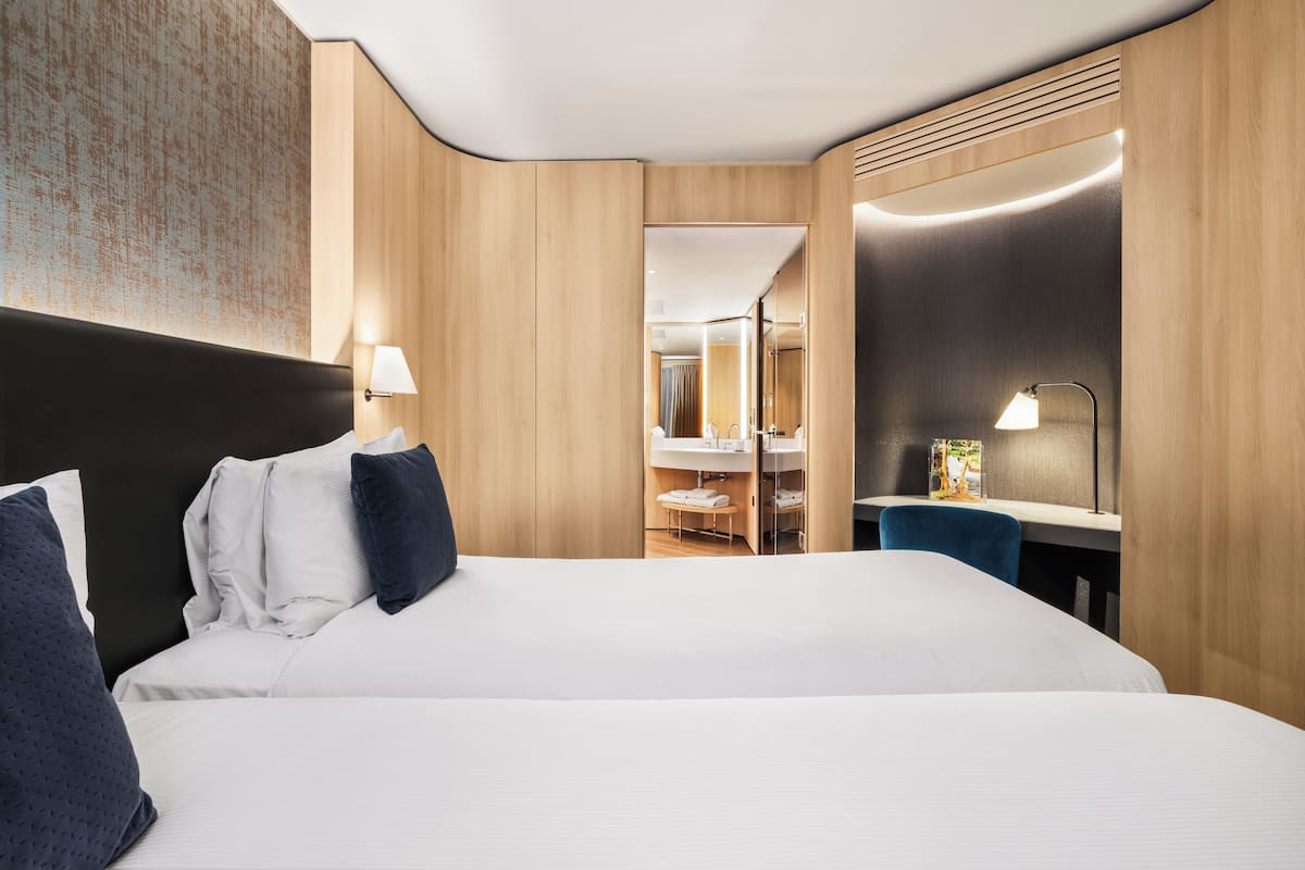 A hotel room with a large bed, a desk, a chair, a mirror, and a bathroom visible through an open door.